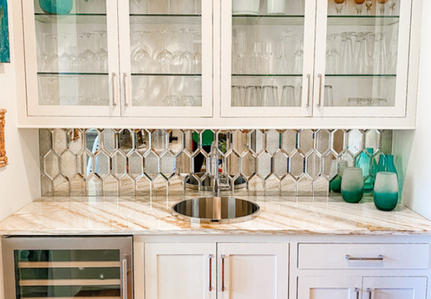 A photo of a white wet bar with honeycomb mirrored backsplash tile